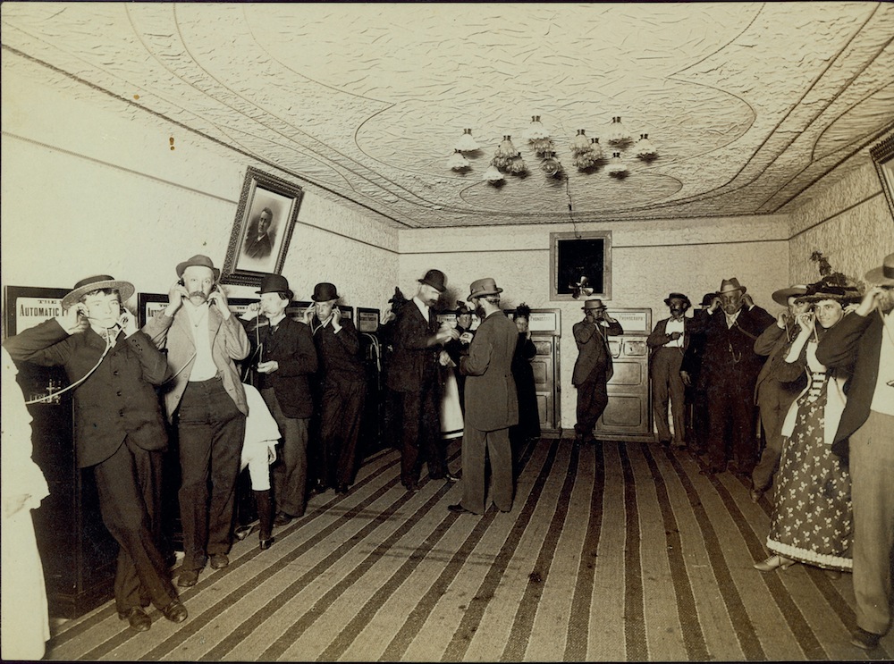 A group of people standing in a room talking on their cell phones.